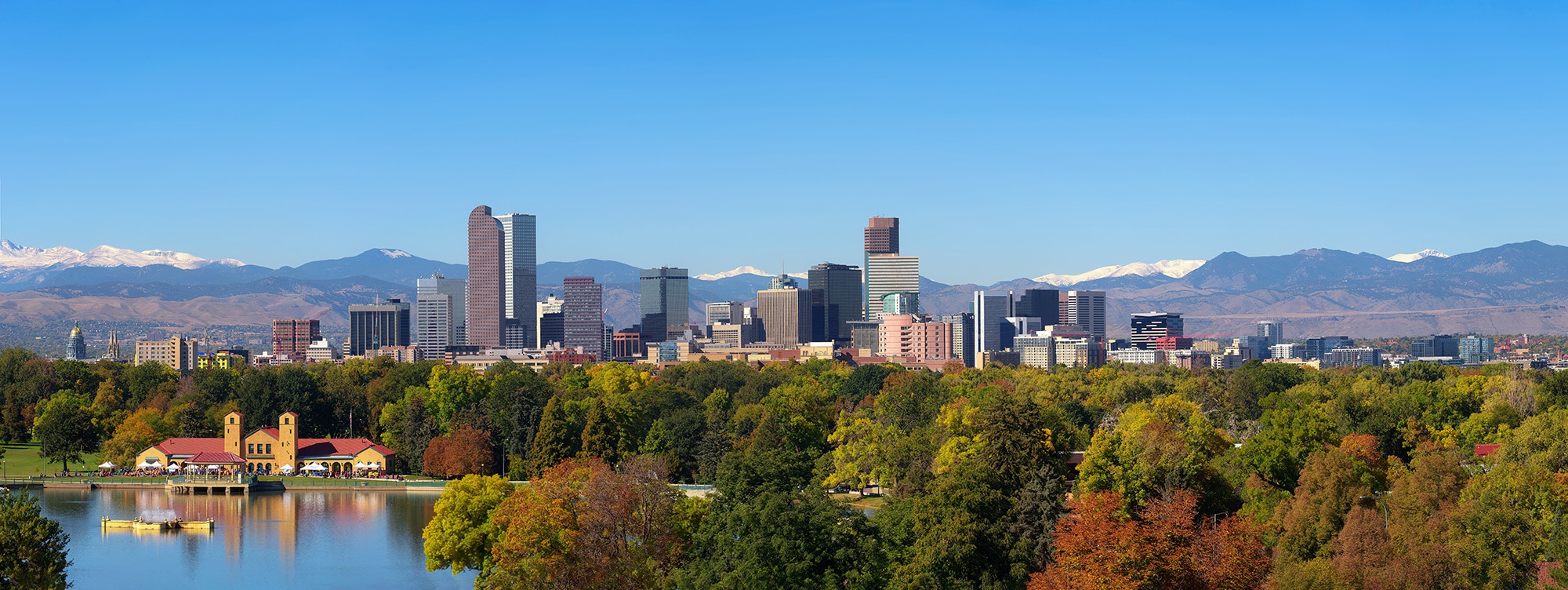 City skyline of Denver Colorado downtown with snowy Rocky Mountains and the City Park Lake. Large panorama.